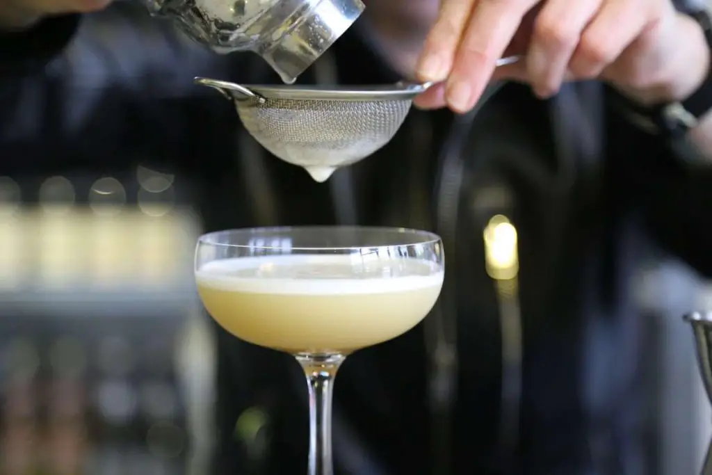 Bartender fine a straining cocktail into a coupe glass