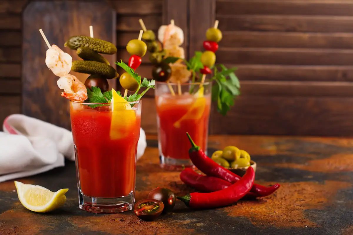 Two bloody mary cocktails garnish with shrimp pickled chili and olives and lime