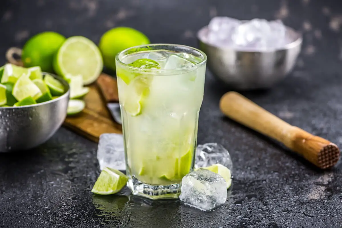 Caipirinha cocktail in a highball glass with lemon wedges and muddler