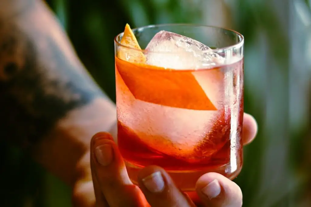 Man with tattoos holding negroni mezcal cocktails
